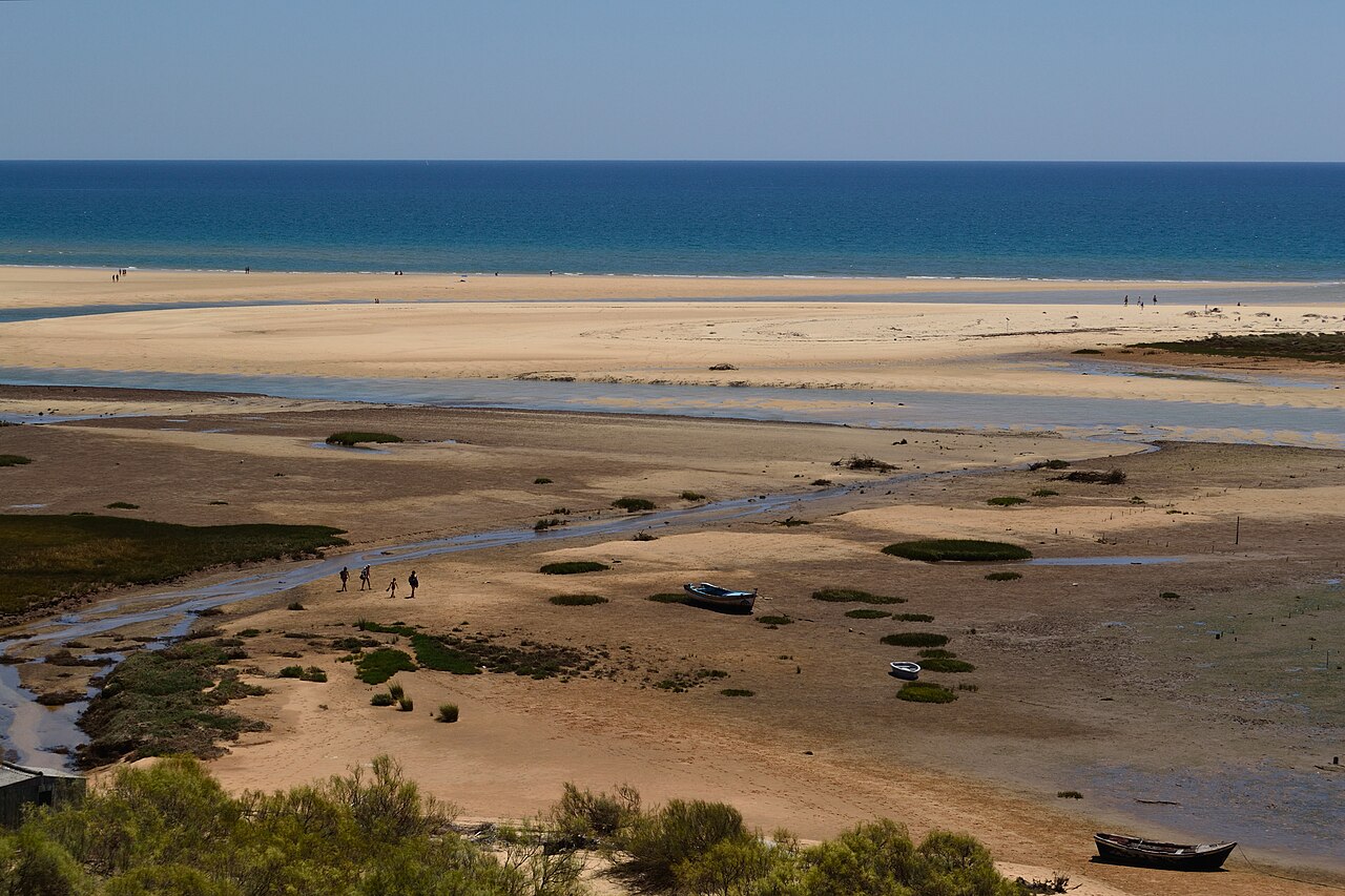 Odpływ pod Cacela Velha: płycizny, łodzie na piasku i mierzeja z plażą od strony oceanu.