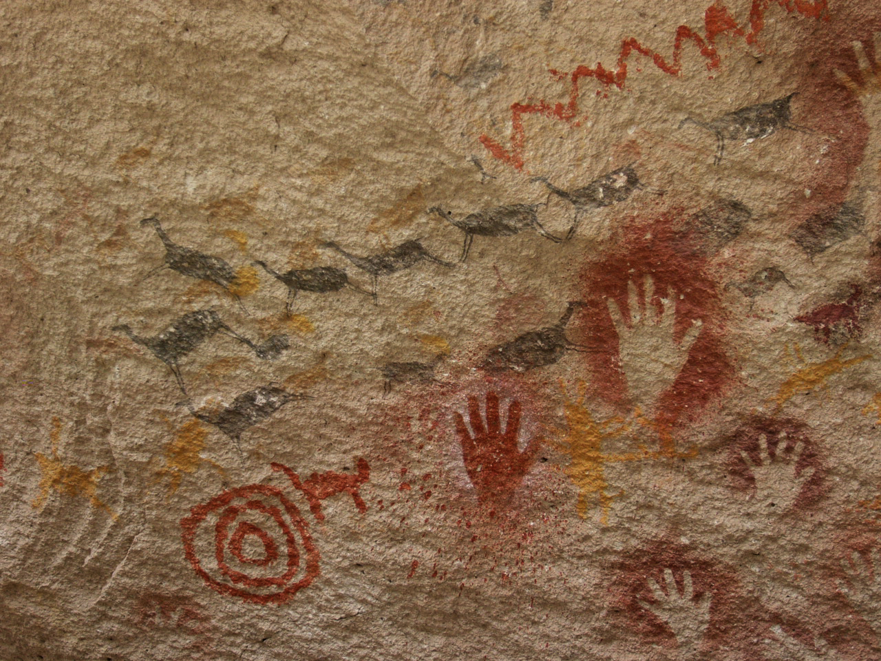 Cueva de las Manos: sylwetki zwierząt, dłonie i spirale namalowane na skale.