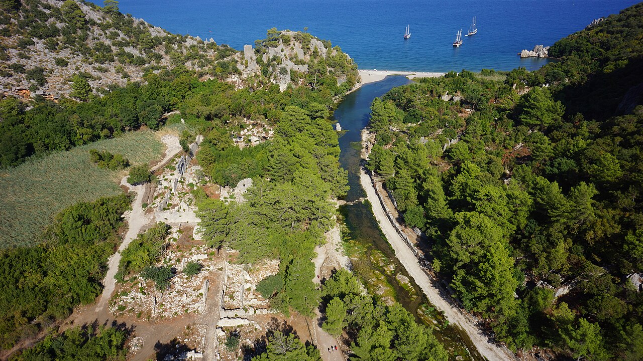 Wąwóz Olympos z lotu ptaka: ruiny w lesie po obu brzegach potoku, w głębi plaża i zatoka